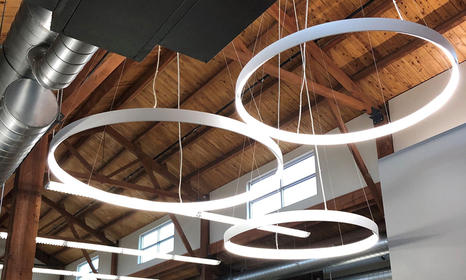 Modern halo pendant lights hanging from an exposed timber ceiling with industrial ductwork.