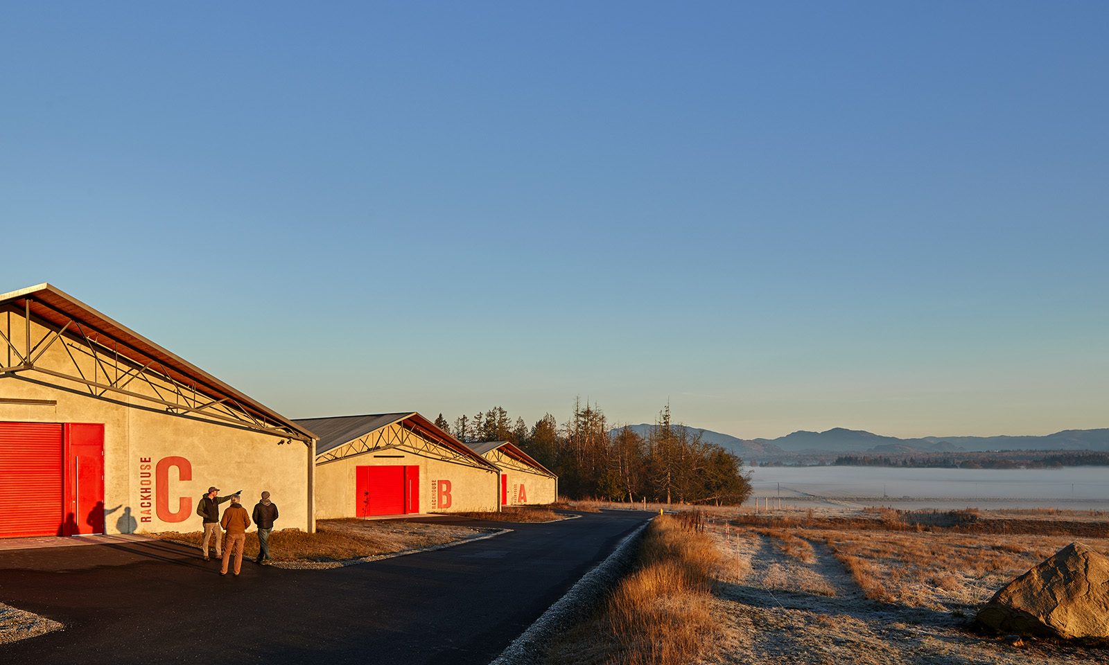 Three concrete rackhouses with red doors in a misty valley landscape, with three people standing outside.