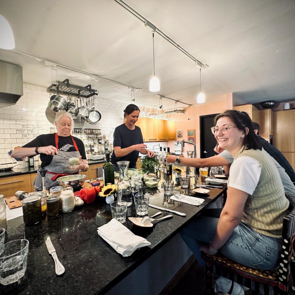 People preparing food and socializing around a large kitchen island during a team cooking event.