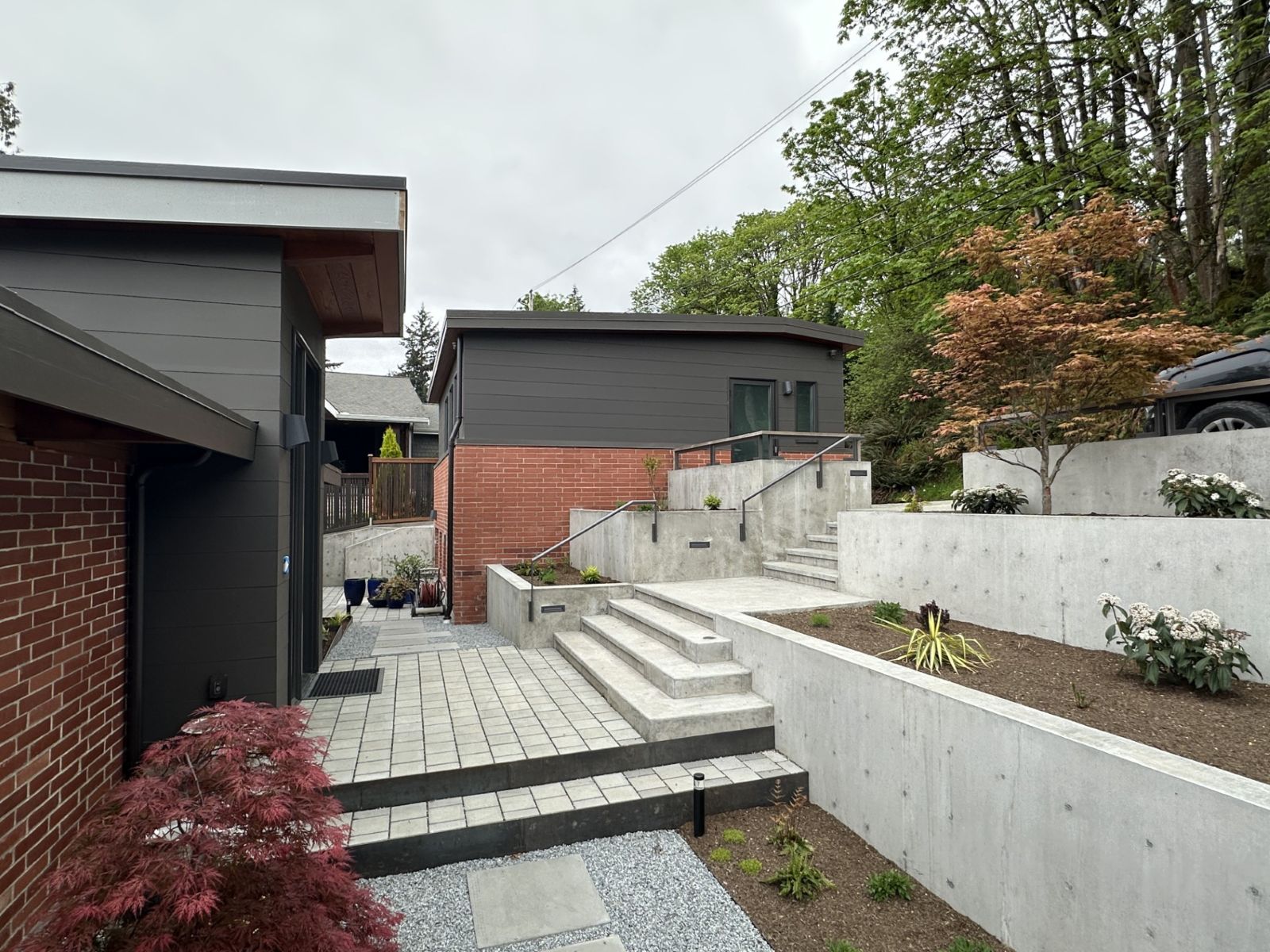Modern backyard with tiered concrete retaining walls, stone steps, and dark grey siding on the home.