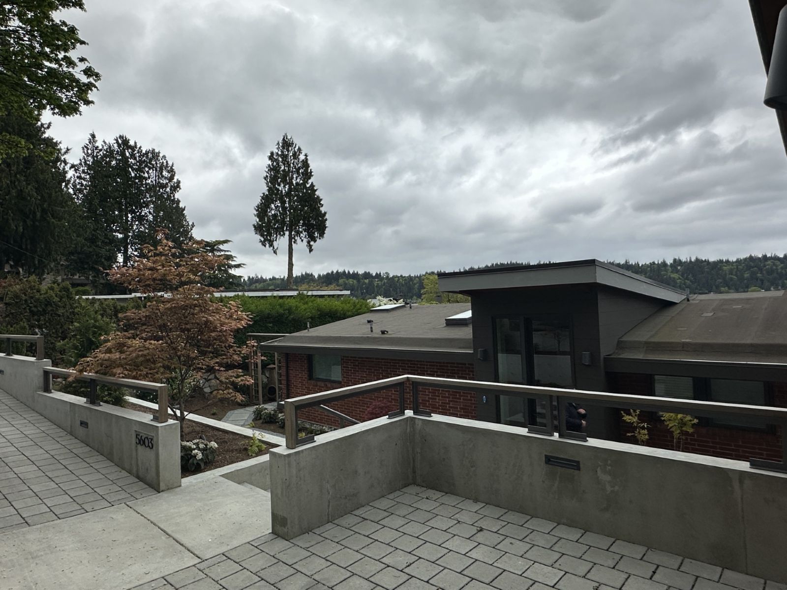 Modern house exterior featuring concrete retaining walls, brick, and dark siding under a cloudy sky.