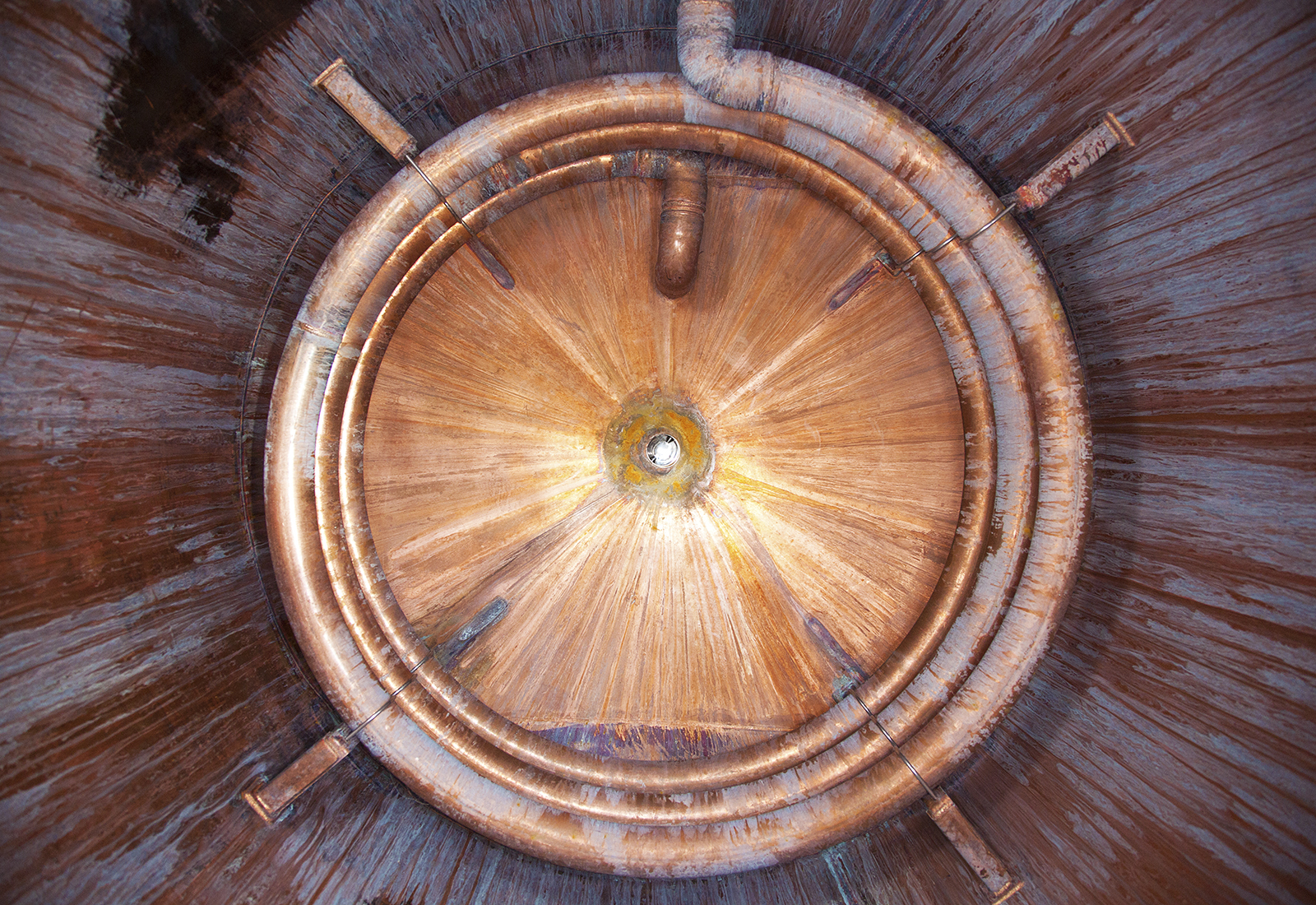 Interior view of a circular copper tank with concentric coils and a weathered, radial metallic texture.