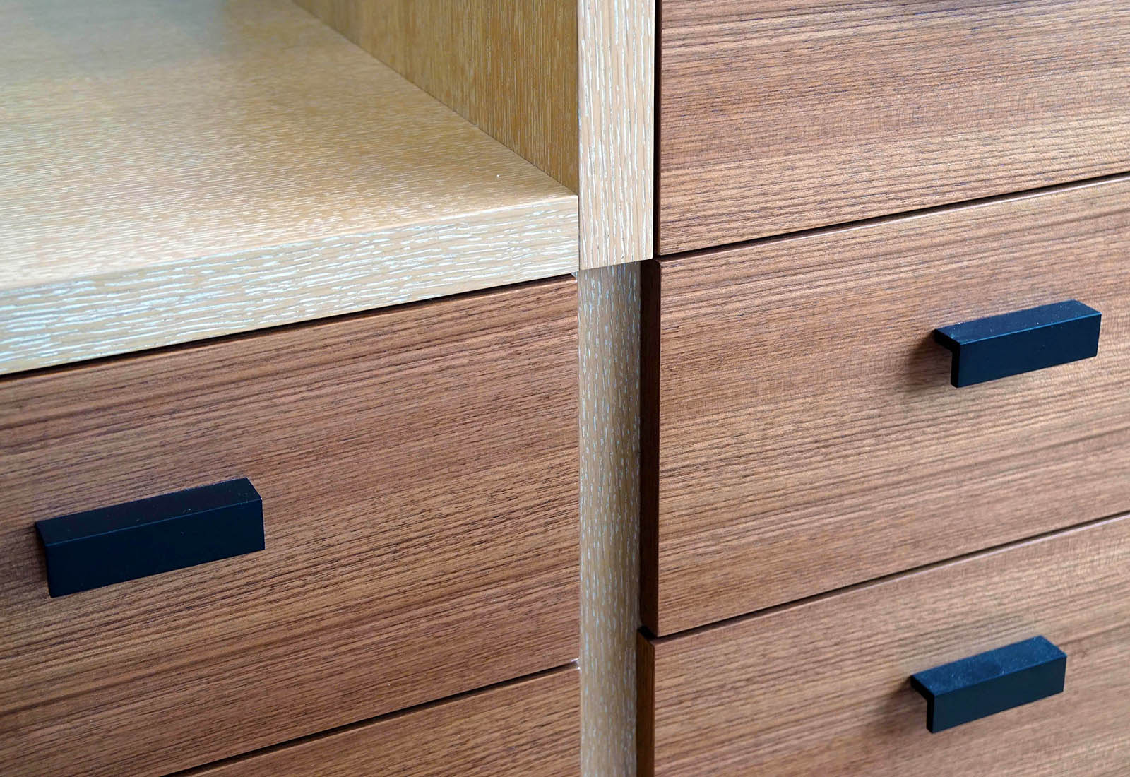 Detail of custom wood cabinets with light oak framing, horizontal grain drawers, and matte black pulls.