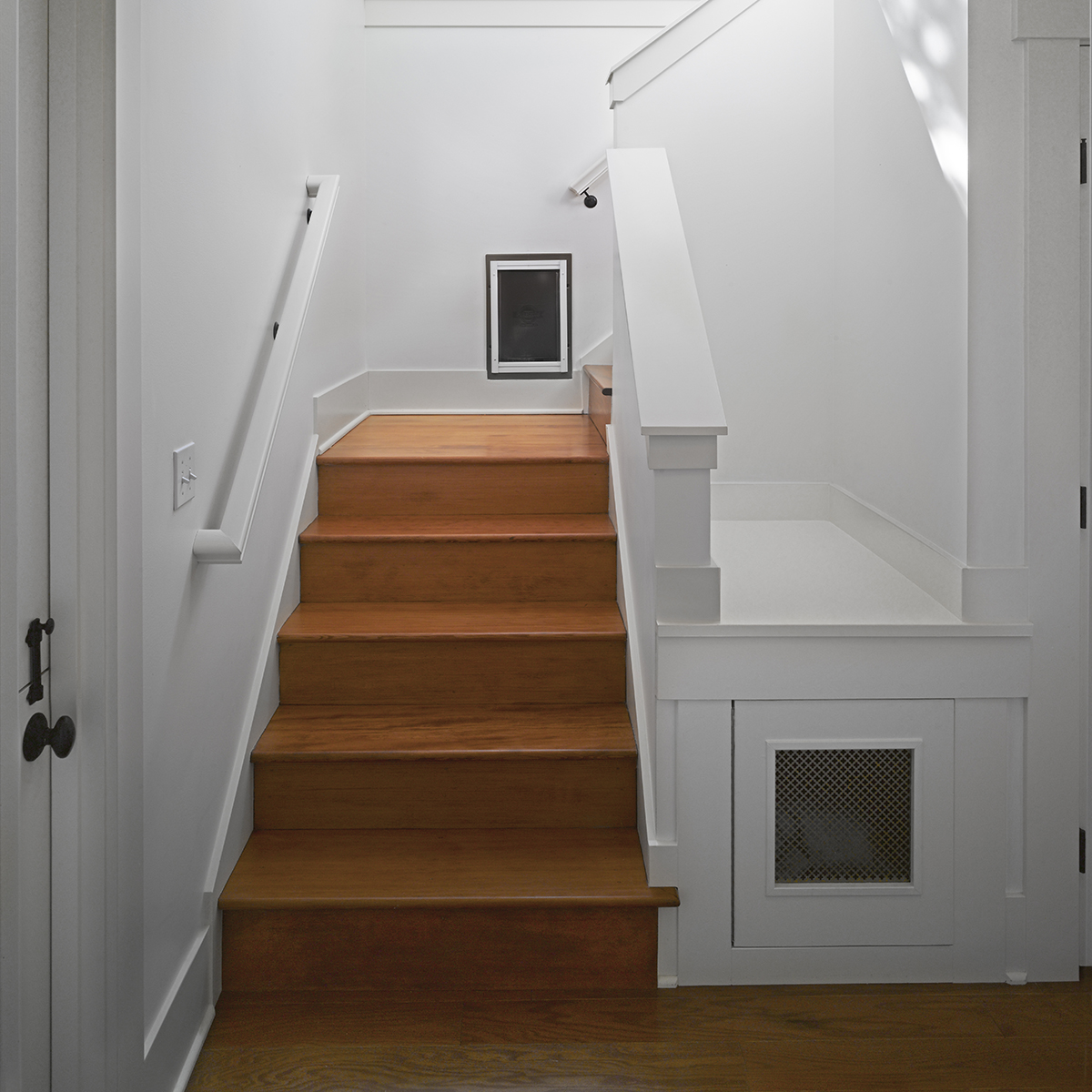 Warm wood stairs with white walls, featuring a custom built-in dog door and integrated under-stair nook.