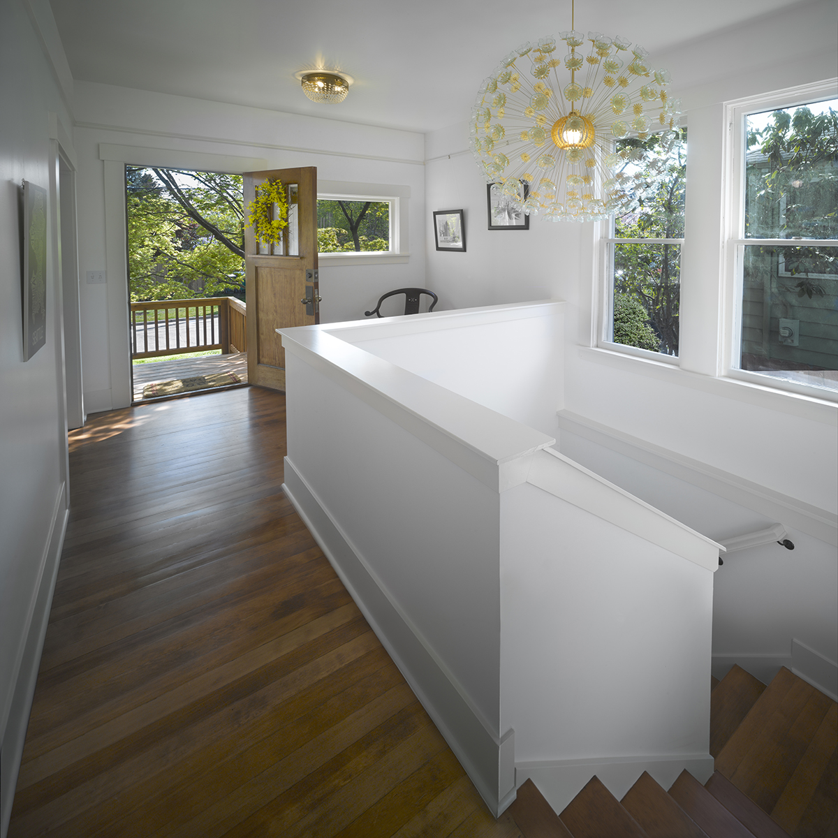 Bright entryway with hardwood floors, an open wooden door to a deck, and a modern dandelion pendant light.
