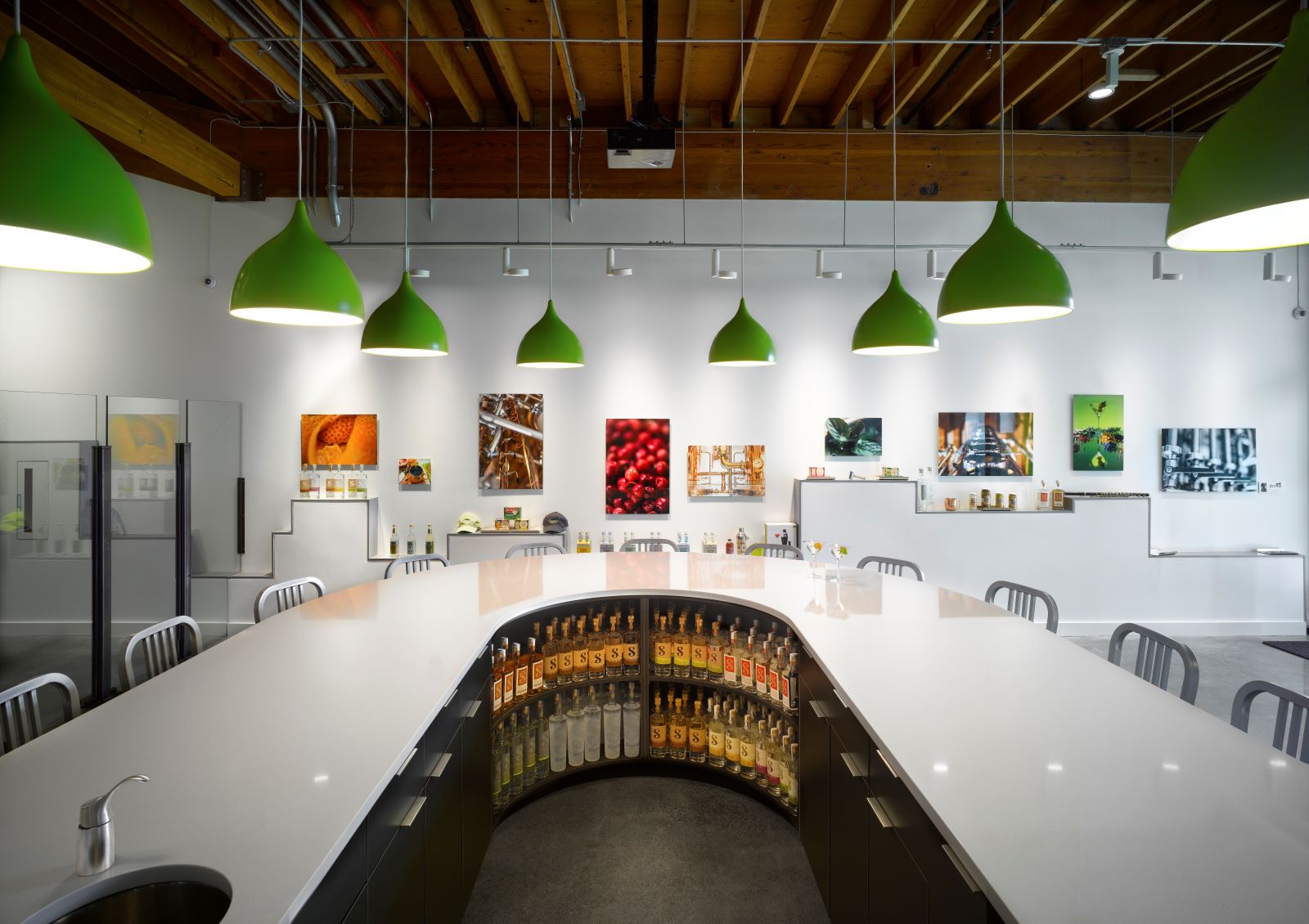 Curved white tasting bar with green pendant lights, exposed wood ceiling, and bottles displayed under the counter