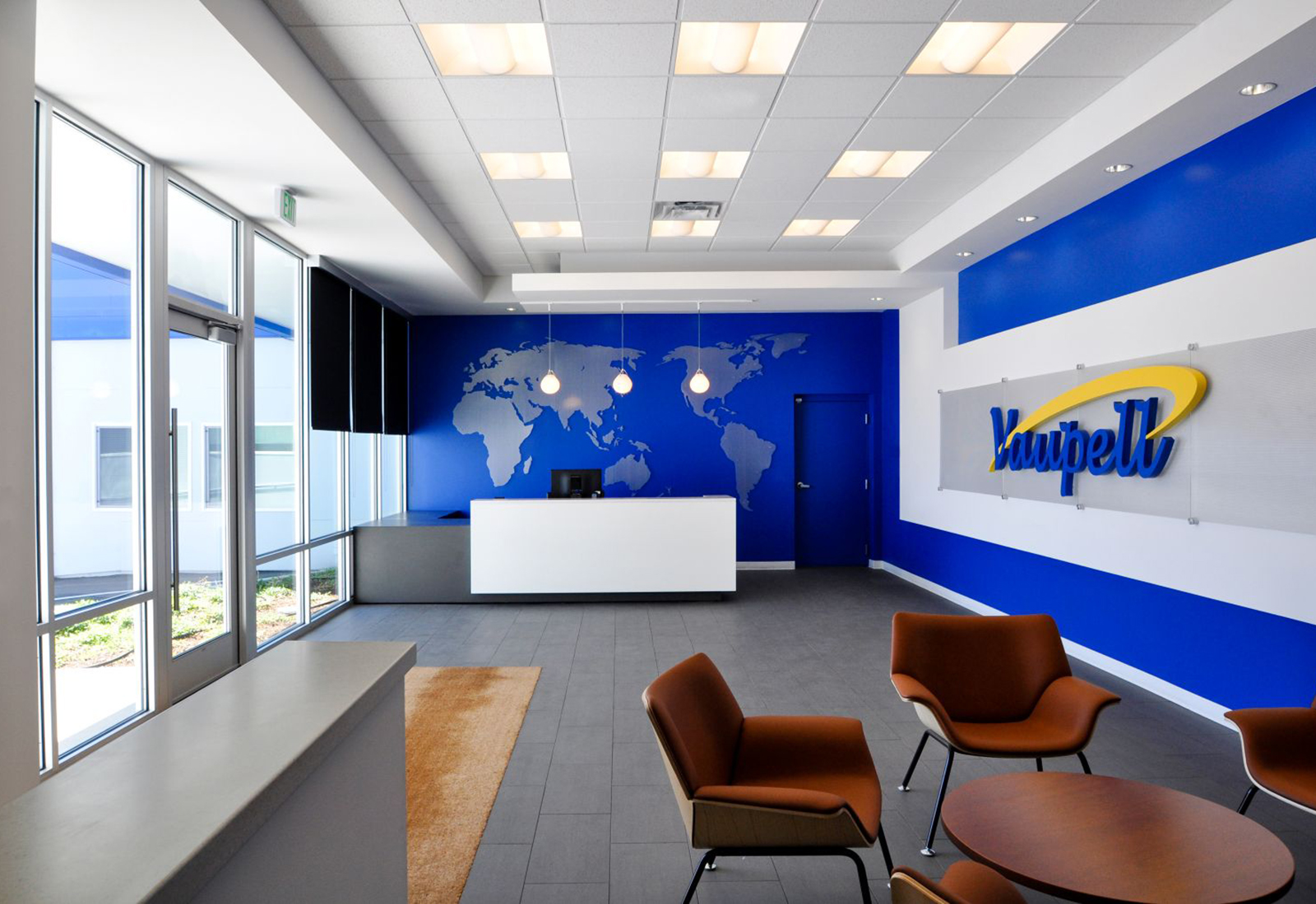 Modern lobby with blue accent walls, a world map graphic behind a white reception desk, and orange armchairs.