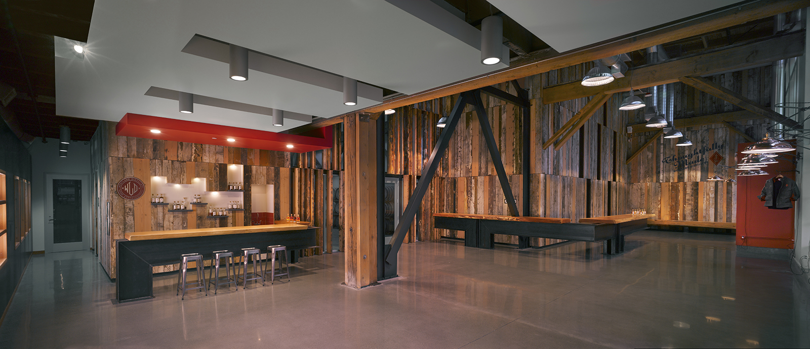 Spacious industrial tasting room with reclaimed wood paneling, polished concrete floors, and steel structural beams.
