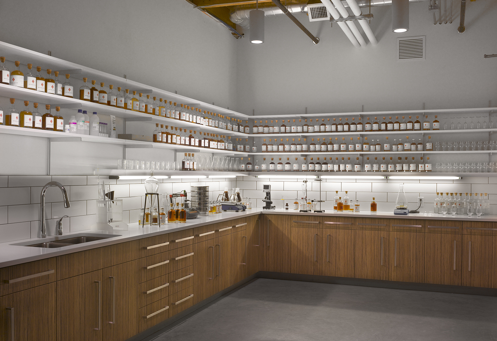 Modern quality control lab with wood cabinets, white subway tile, and shelves lined with glass sample bottles.