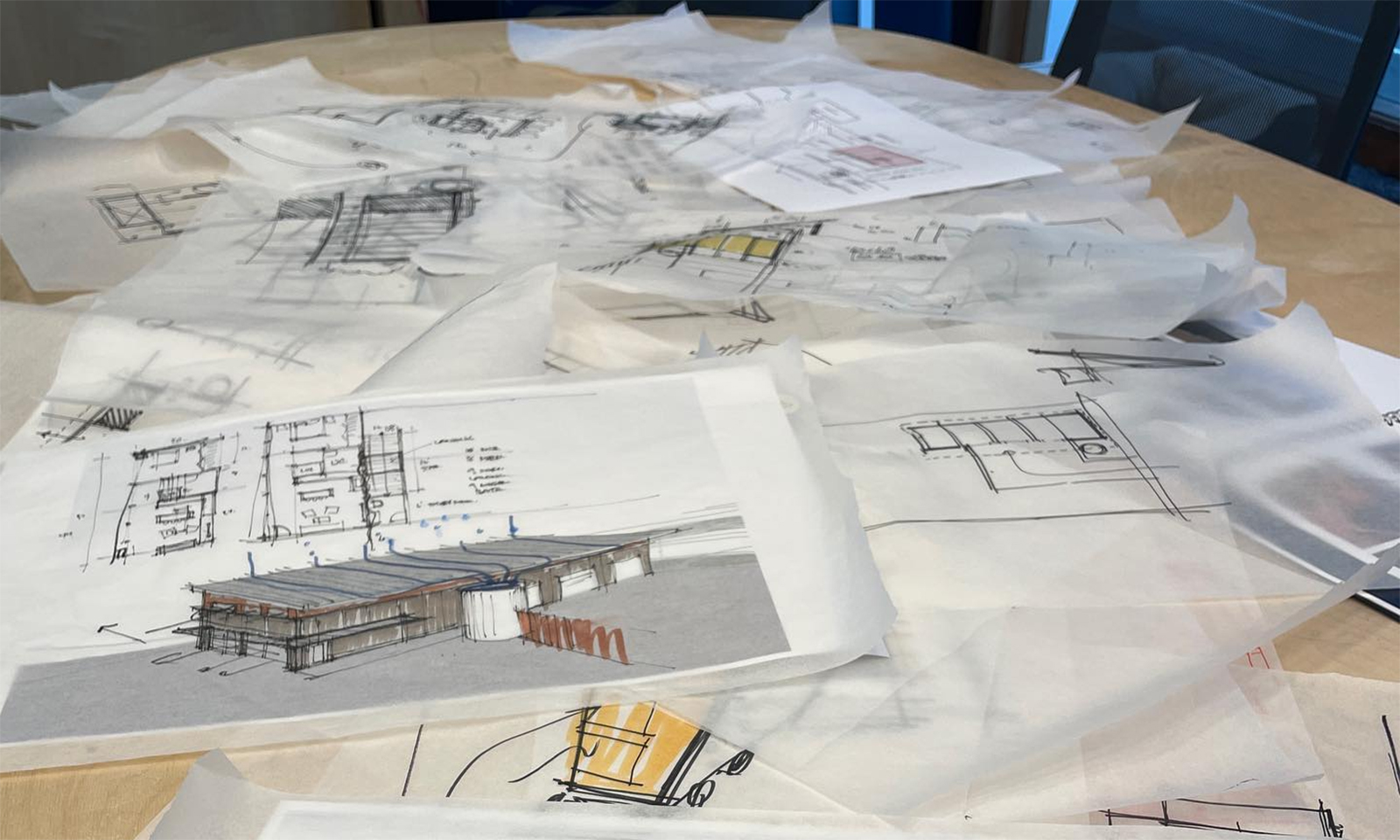 Architectural concept sketches and tracing paper drawings scattered on a wooden work table.