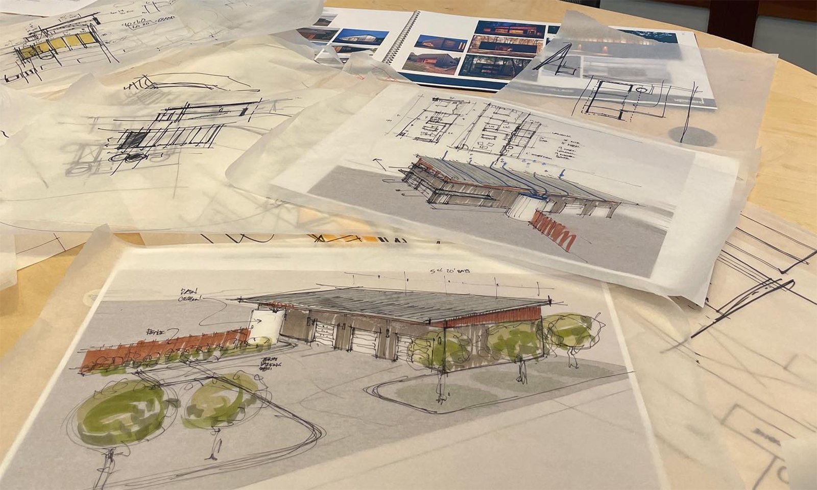Architectural sketches, floor plans, and hand-drawn building renderings on tracing paper spread across a table.
