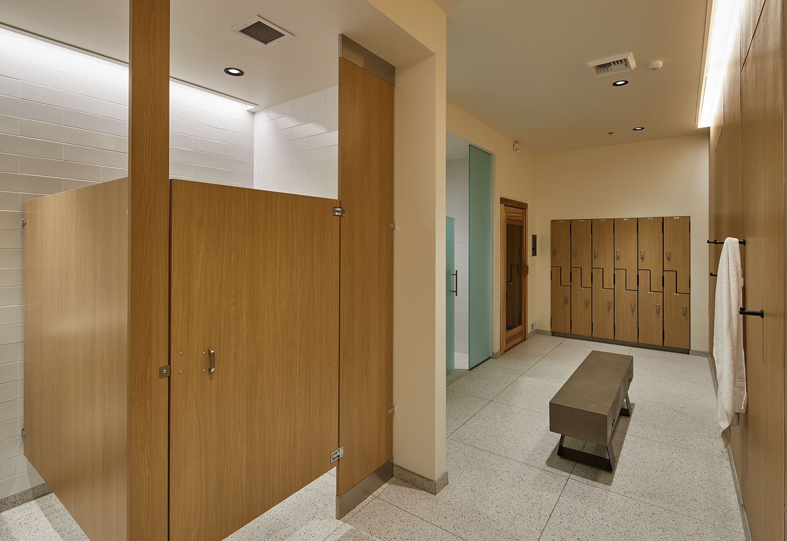 Modern locker room with light wood stalls, a concrete bench, and minimalist wooden lockers.