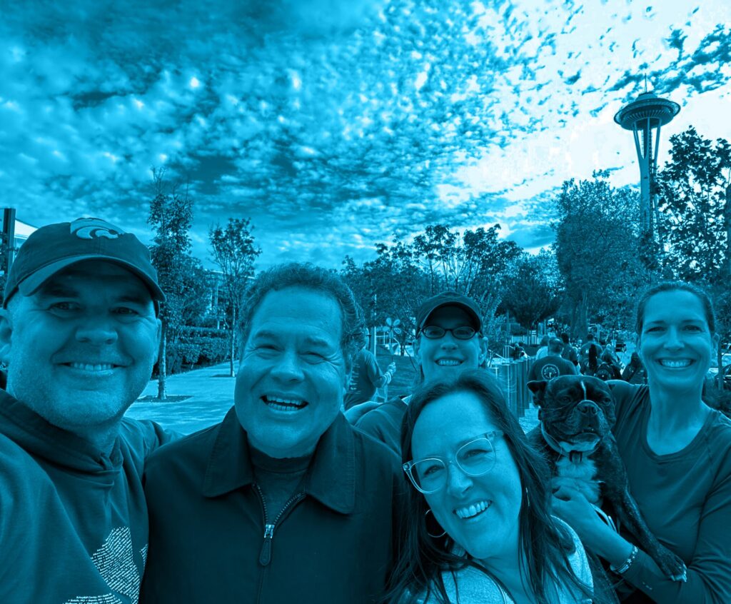 Smiling group selfie with a dog in Seattle, with the Space Needle in the background under a blue filter.