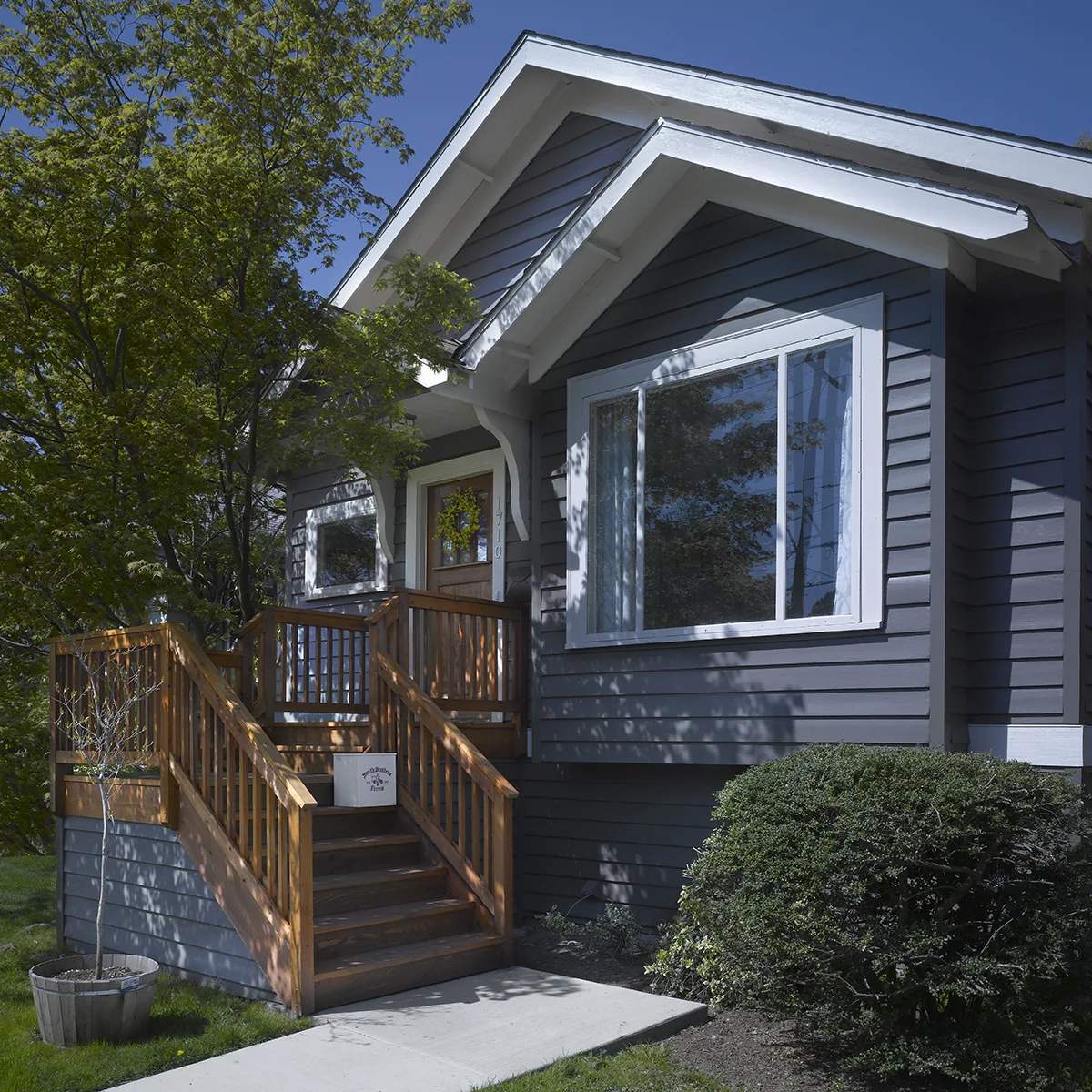 Dark grey craftsman home exterior with white trim, a wooden front porch, and lush green landscaping.