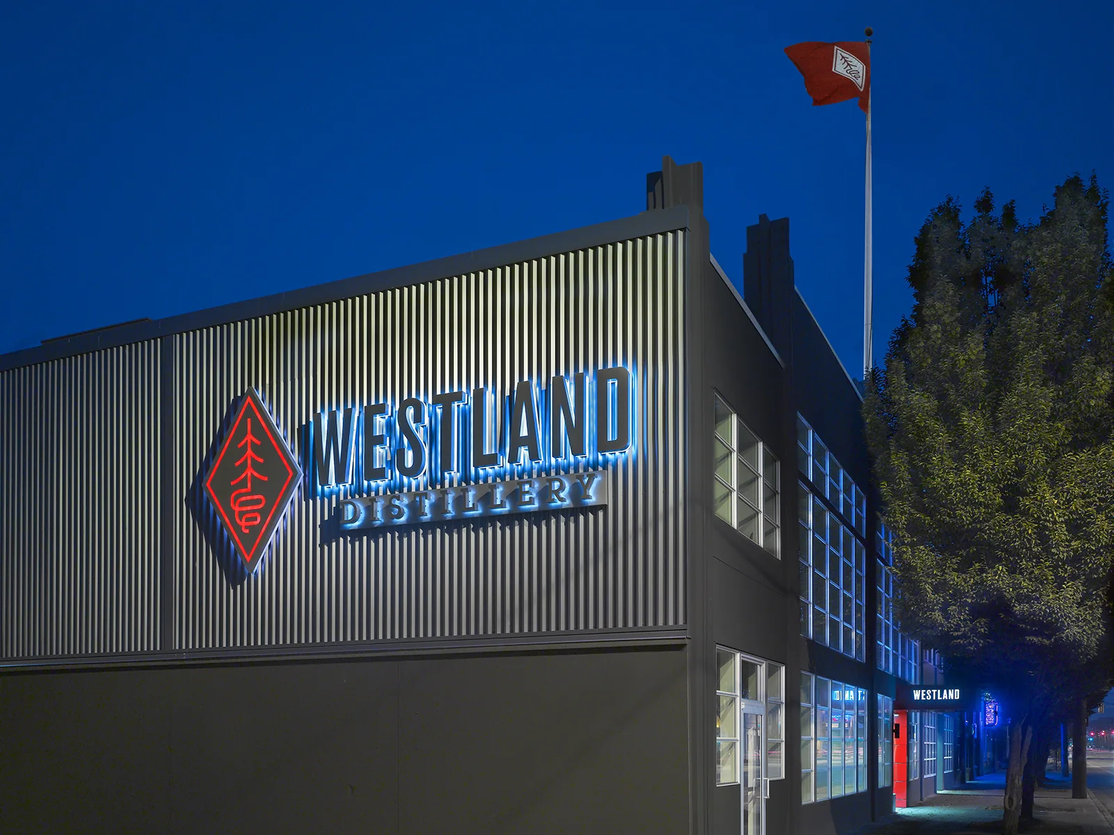 Glowing blue neon sign on the corrugated metal exterior of Westland Distillery at dusk.