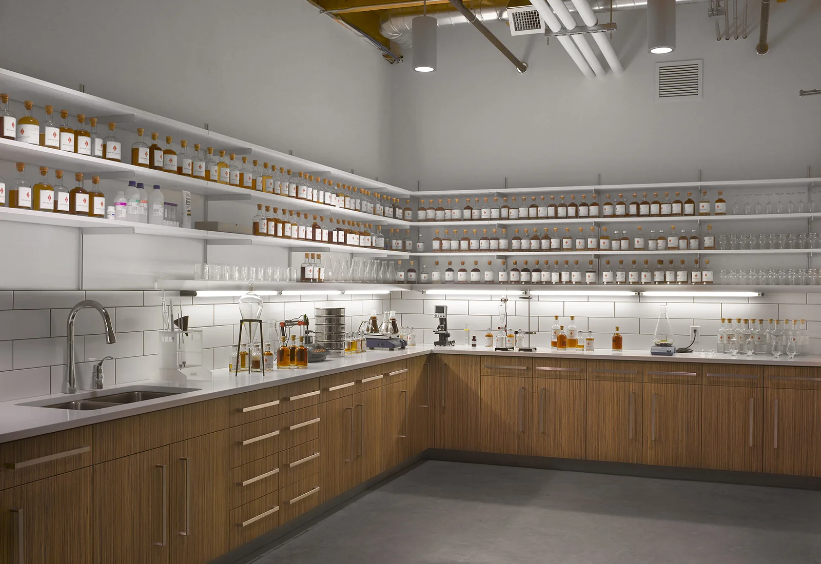 Modern quality control lab with wood cabinets, white subway tile, and shelves lined with glass sample bottles.