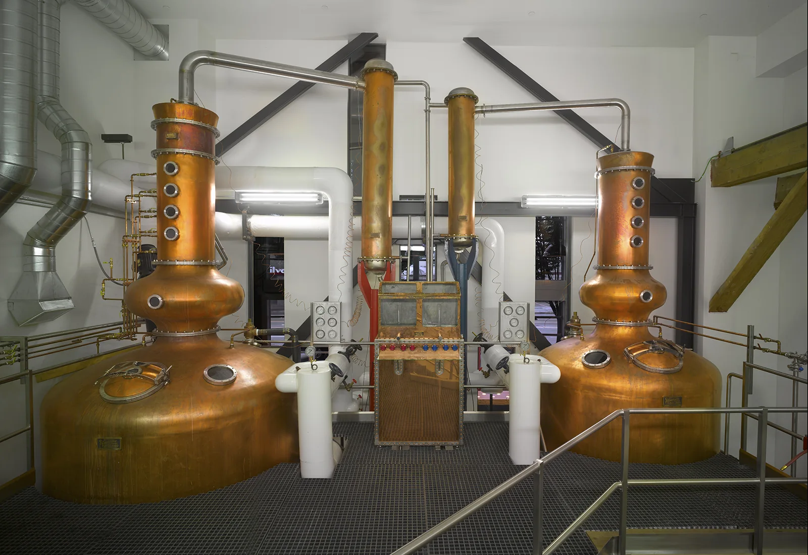 Two large copper pot stills connected by steel pipes in a modern, industrial distillery.