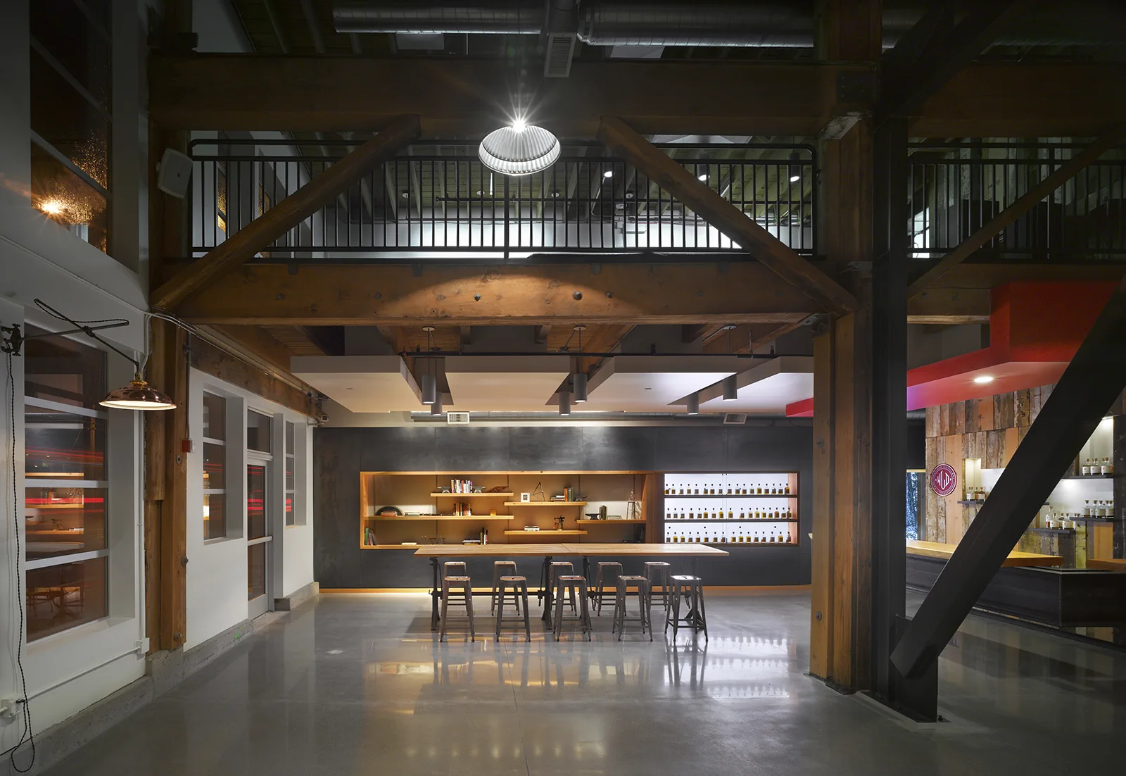 Industrial tasting room with heavy timber beams, polished concrete floors, and a long wooden table with stools.