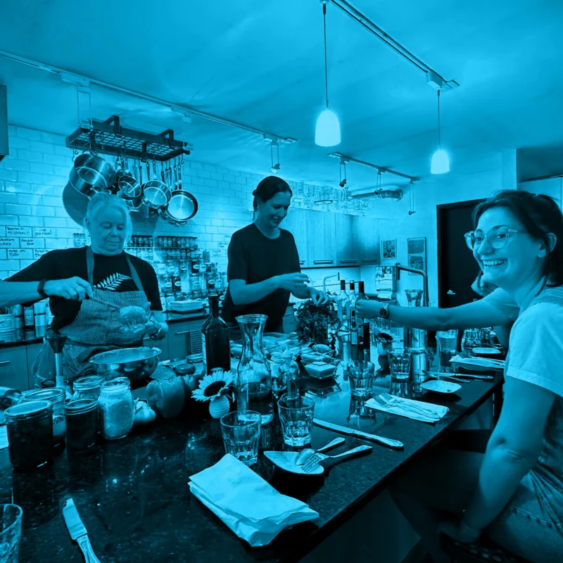 People preparing food around a kitchen counter during a team-building event, shown with a blue color filter.