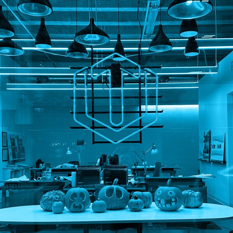 Jack-o'-lanterns displayed on a table inside a modern office illuminated by cool blue light.