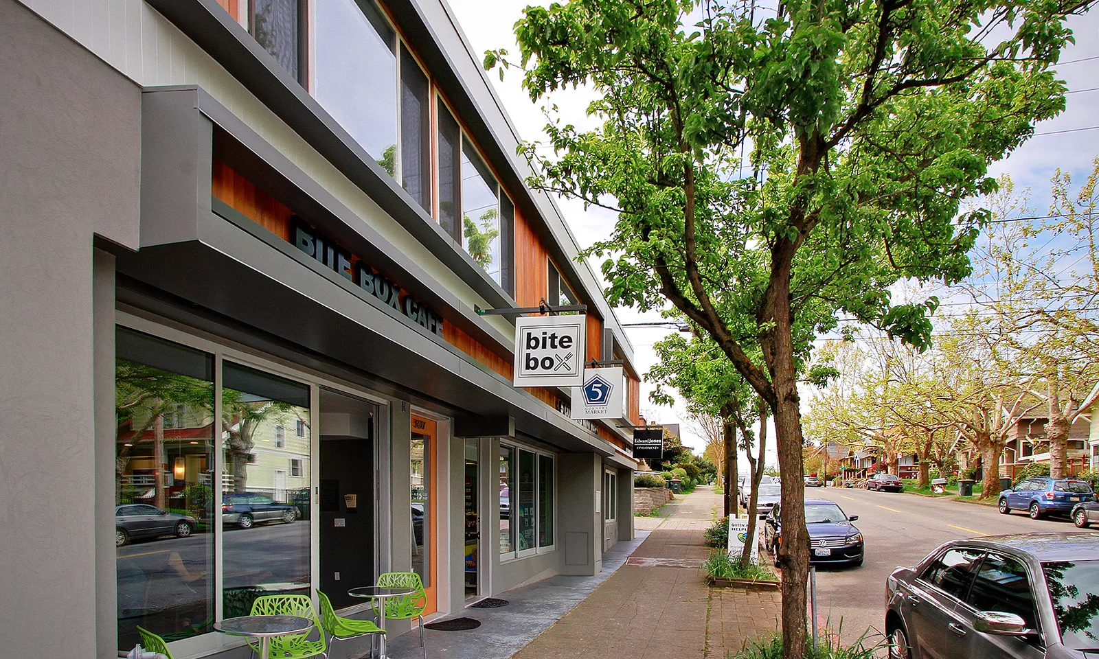 Modern storefront with wood paneling, large windows, and outdoor seating on a tree-lined neighborhood street.