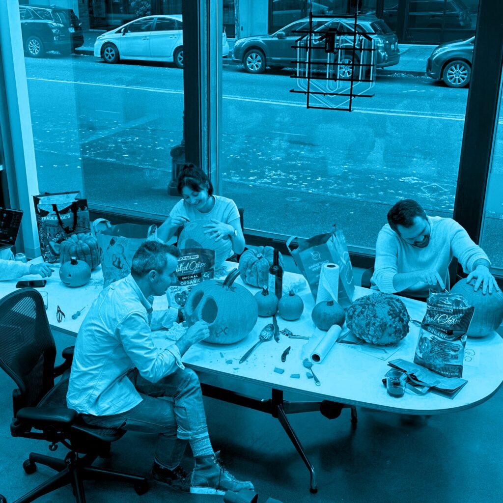 People carving pumpkins around an office conference table, shown with a bright blue color overlay.