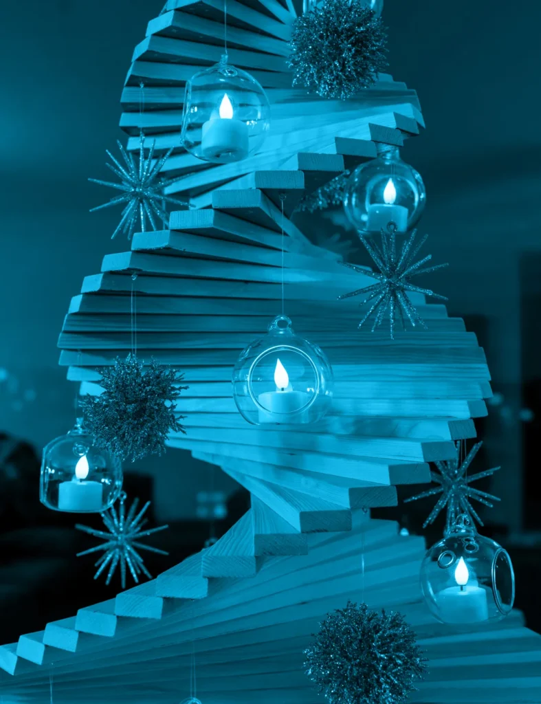 Spiral wooden holiday tree decorated with hanging glass candle globes and starburst ornaments in blue light.