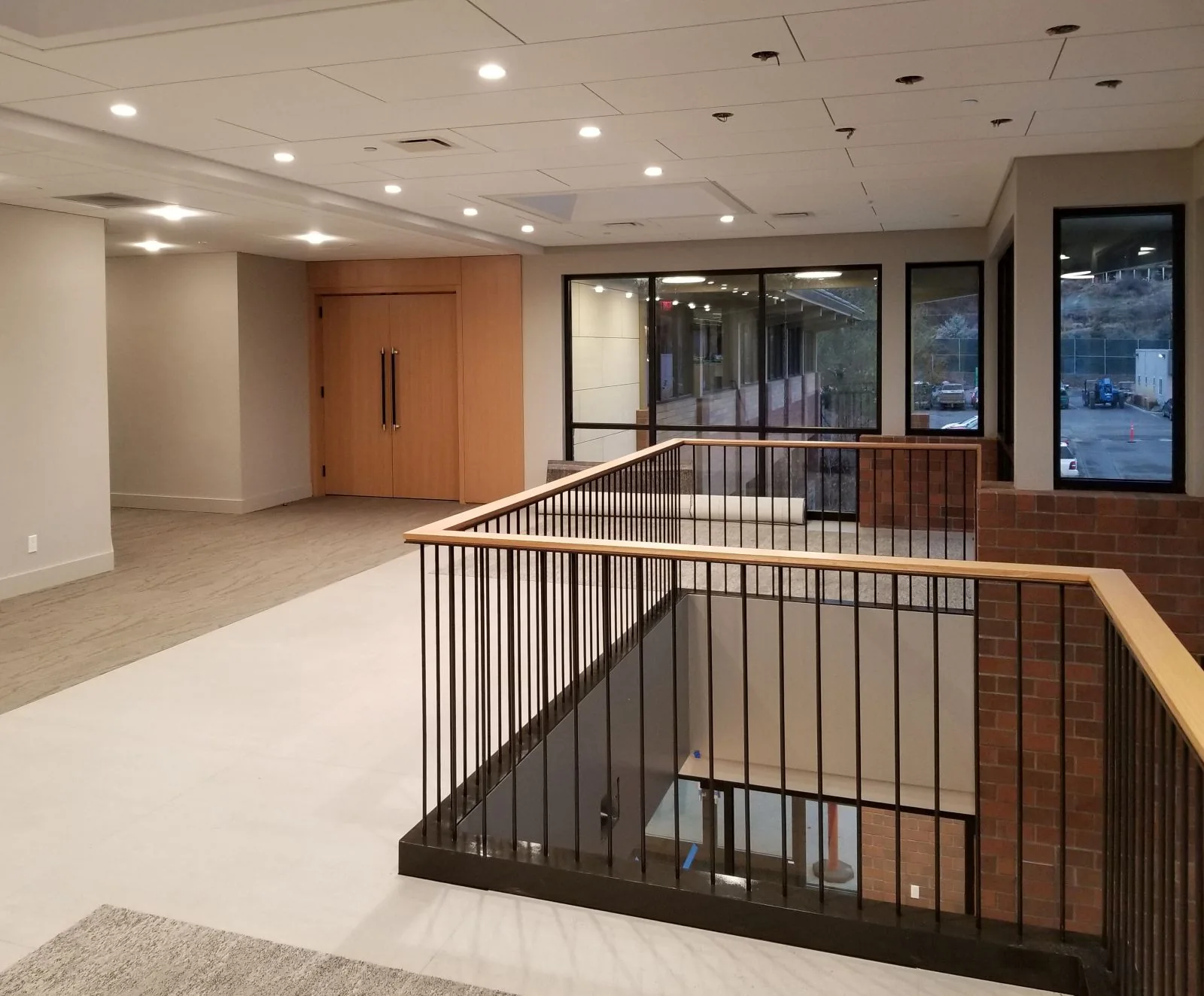 Modern mezzanine with black metal railings, brick accents, large windows, and recessed ceiling lights.
