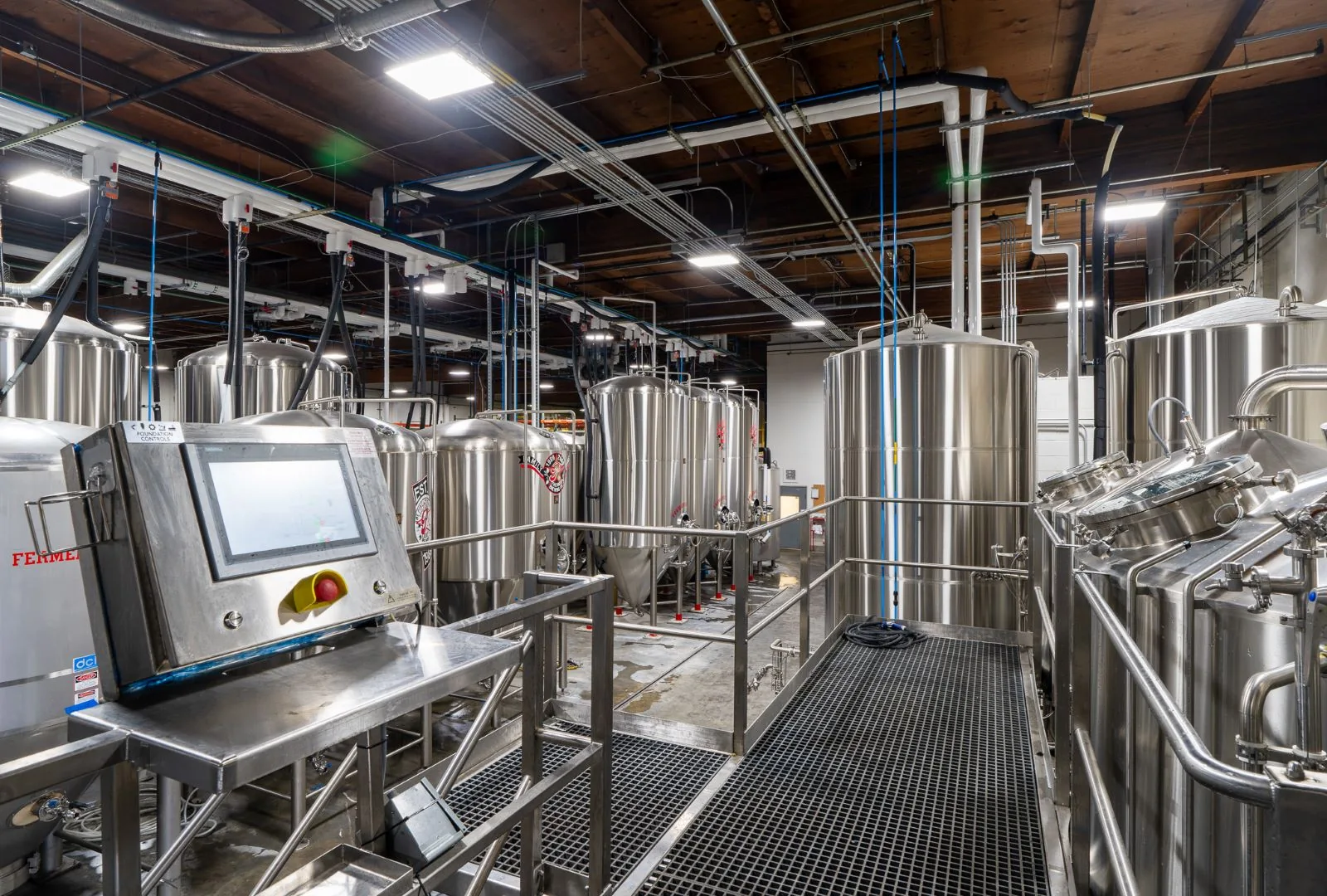 Stainless steel fermentation tanks and a digital control panel inside a modern industrial brewery.