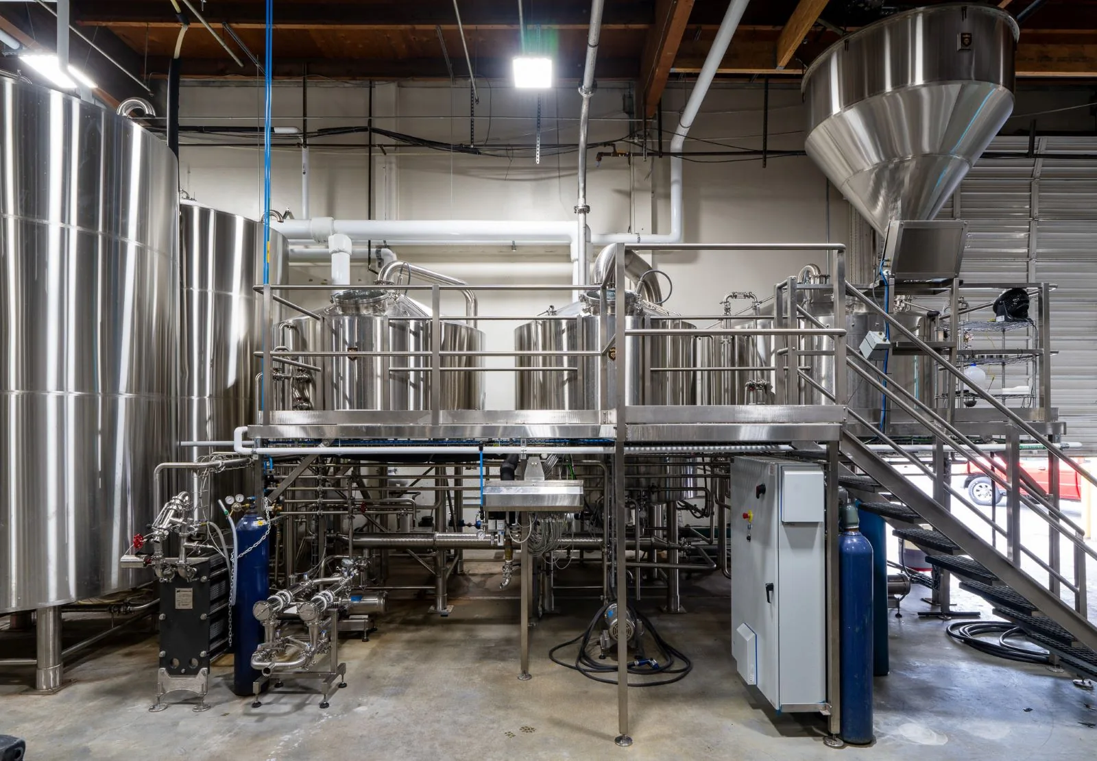 Stainless steel brewing tanks and equipment on a raised platform in an industrial brewery.