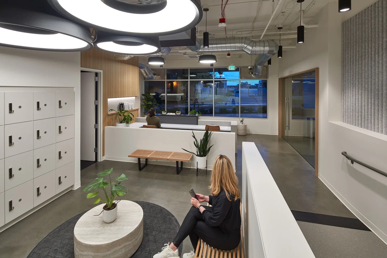 Modern lobby with white lockers, concrete floors, large circular light fixtures, and minimalist seating.