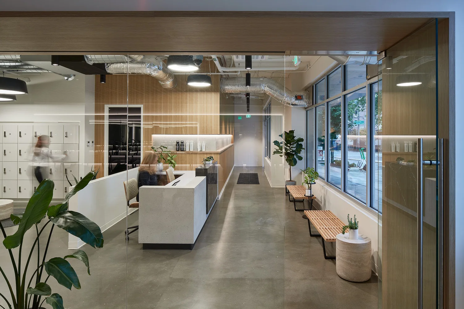 Modern office reception area with concrete floors, wood-paneled walls, a white desk, and large windows.