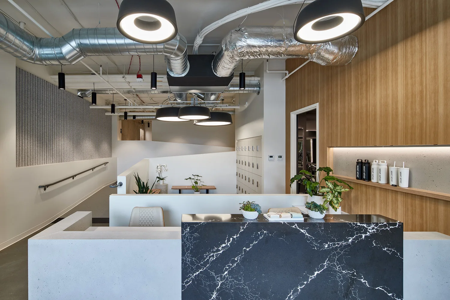Modern reception area with a black marble desk, concrete accents, wood paneling, and exposed industrial ductwork.