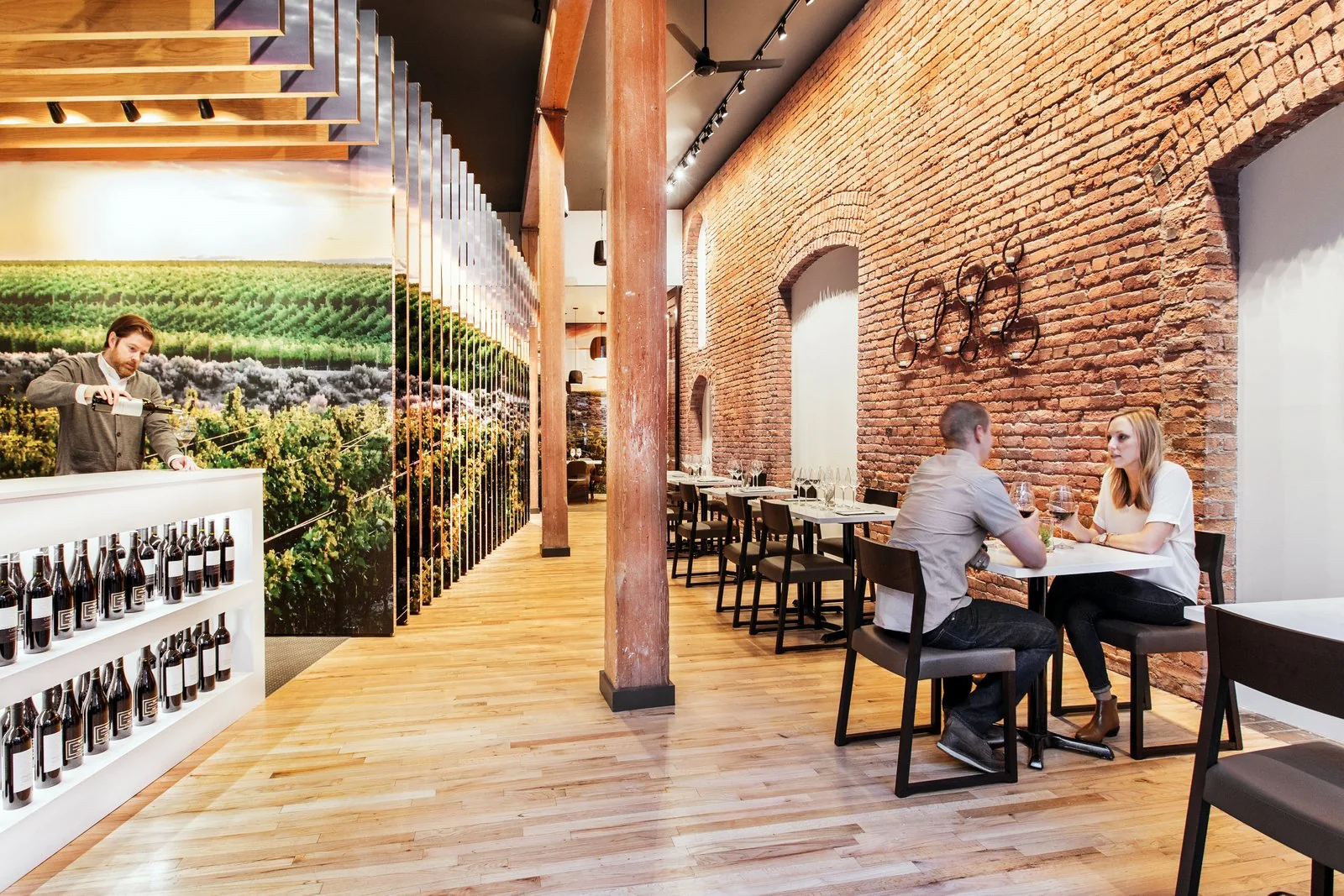 Wine tasting room with an exposed brick wall, timber columns, wood floors, and a large vineyard mural.
