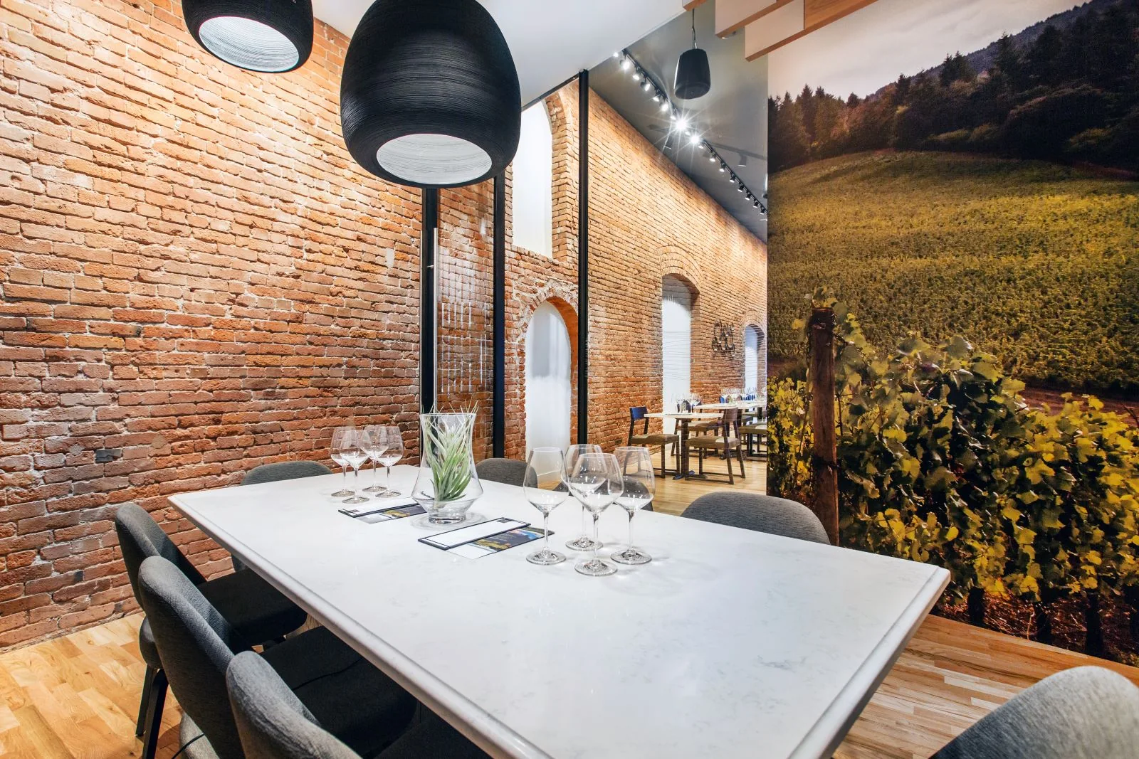 Modern wine tasting room with a white marble table, exposed brick walls, and a large vineyard wall mural.