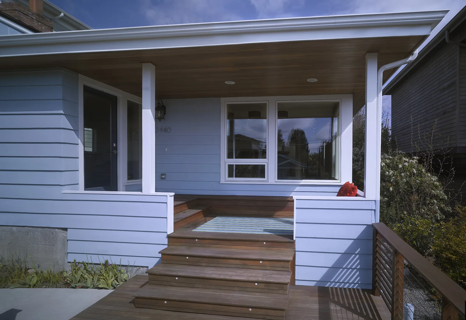 Modern front porch with light blue siding, wooden steps, a warm wood ceiling, and white trim.