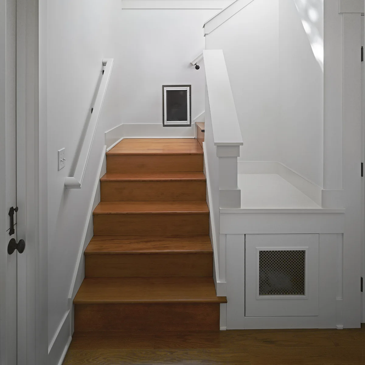 Warm wood stairs with white walls, featuring a custom built-in dog door and integrated under-stair nook.