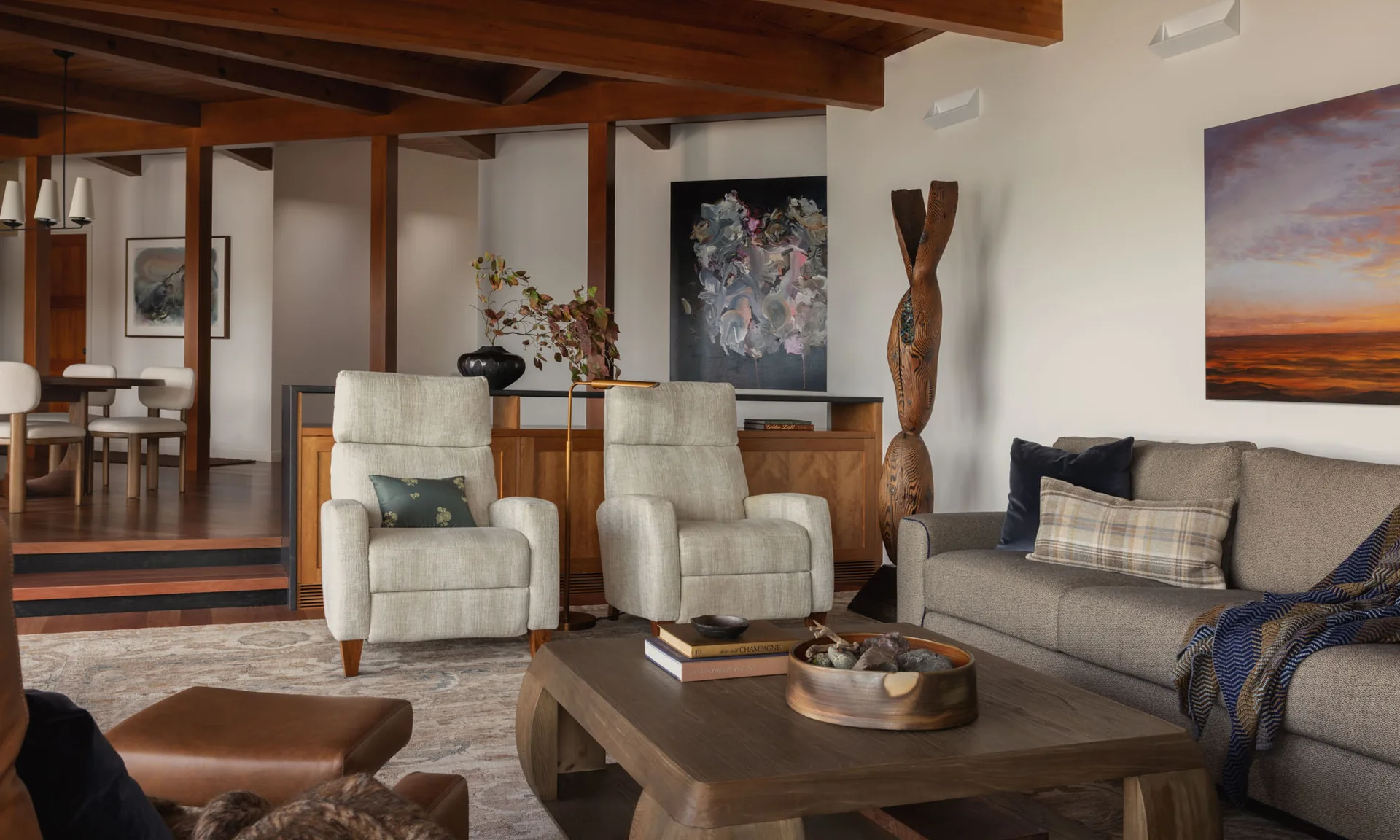 Cozy mid-century modern living room with exposed wood ceiling beams, a grey sofa, and two light armchairs.