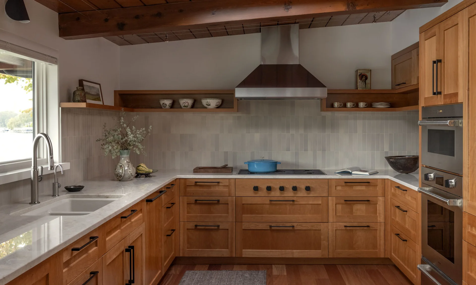 Modern kitchen with warm wood cabinets, white countertops, vertical tile backsplash, and exposed ceiling beams.