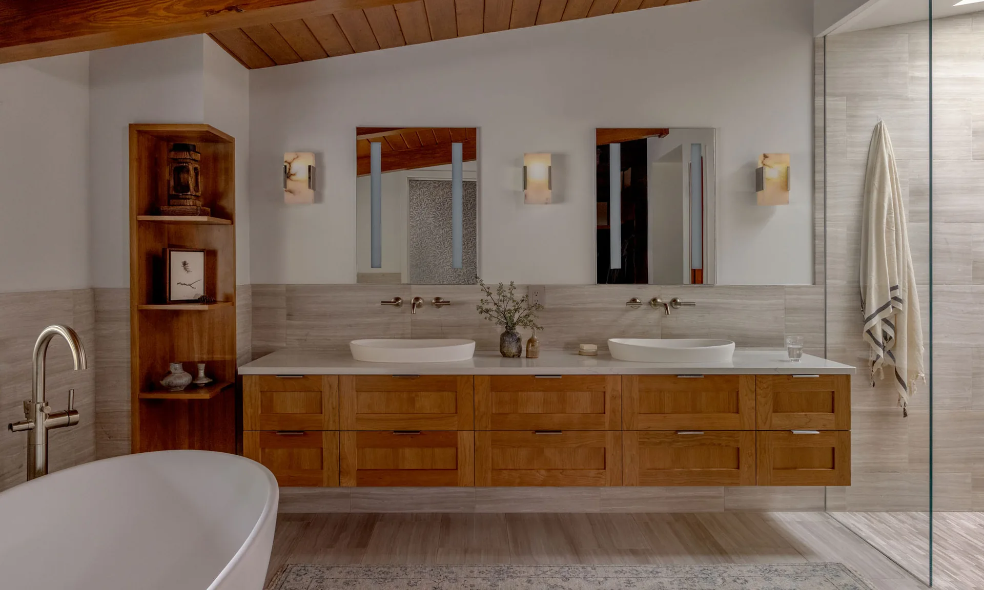 Modern bathroom with a floating wood double vanity, white vessel sinks, freestanding tub, and warm wood ceiling.