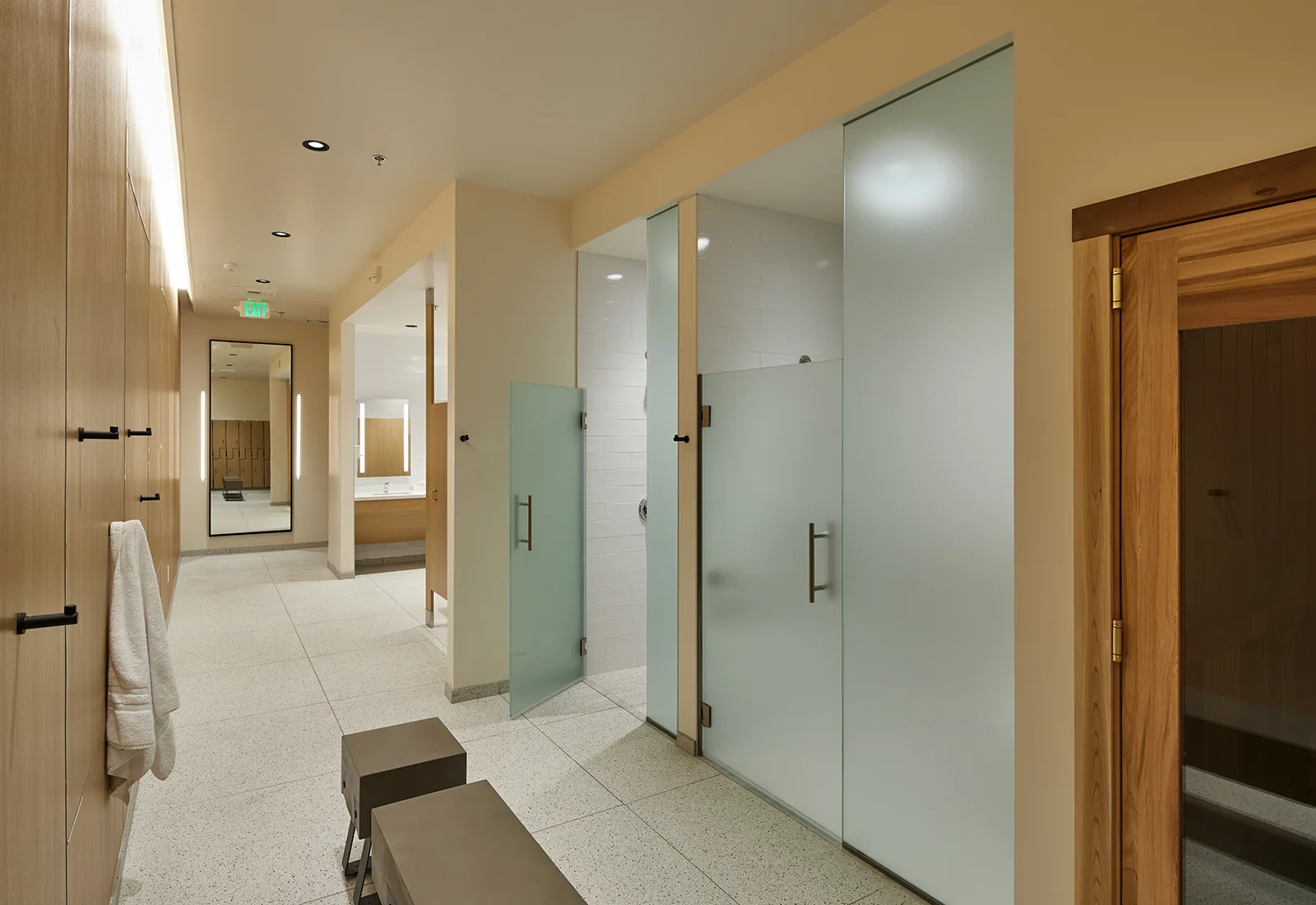 Modern spa locker room with frosted glass shower stalls, light wood lockers, and minimalist benches.