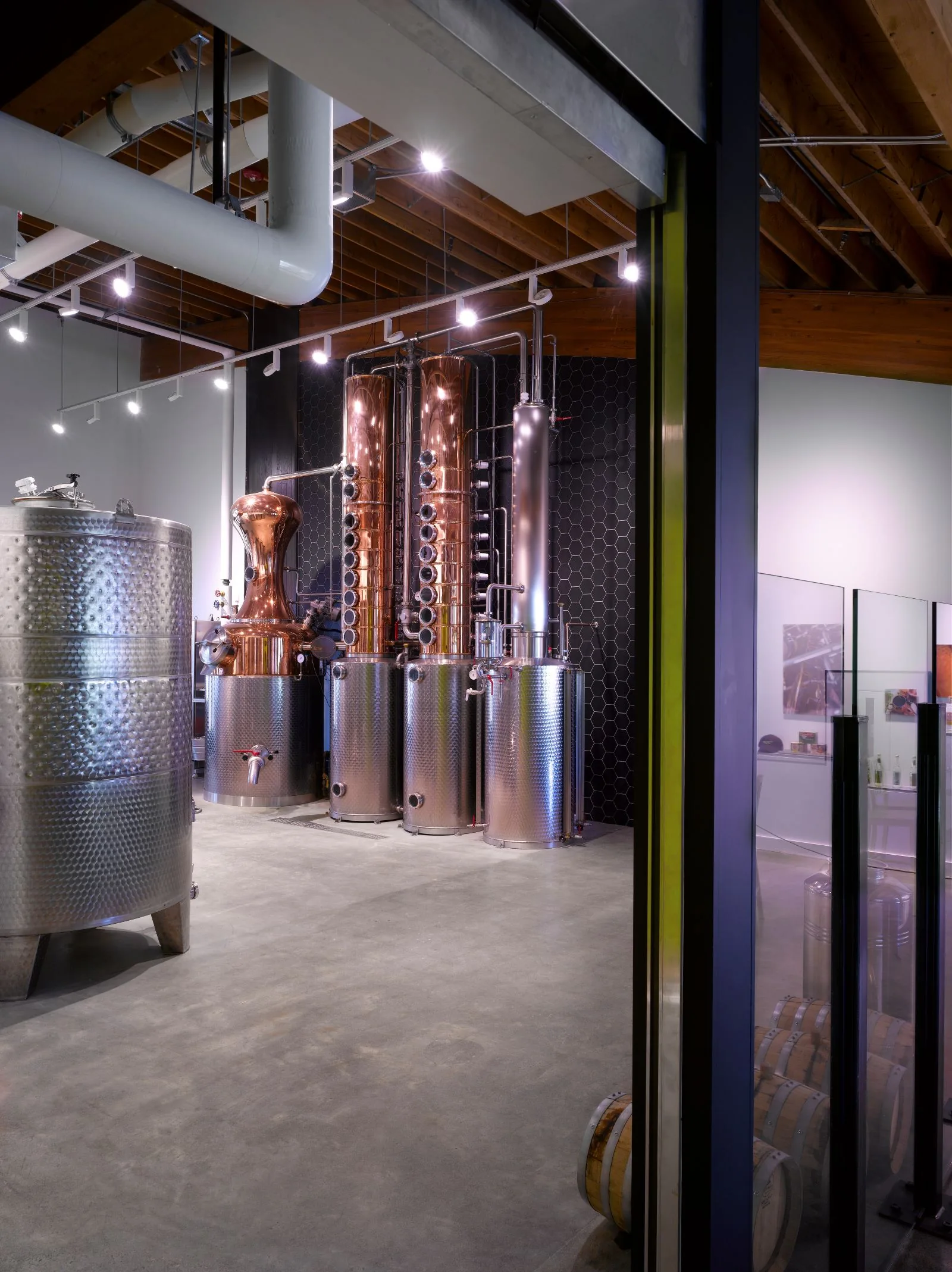 Industrial distillery room with copper and stainless steel stills, concrete floors, and exposed wood ceiling.