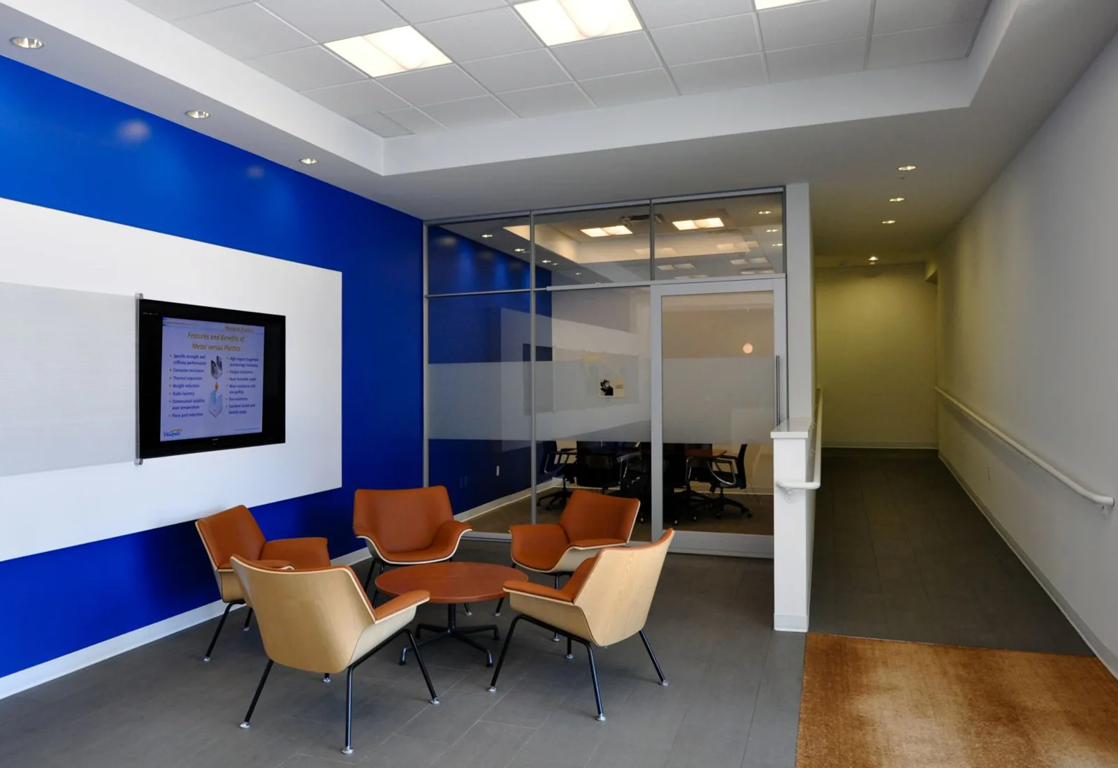 Modern office lobby featuring orange armchairs, a vibrant blue accent wall, and a glass-walled conference room.