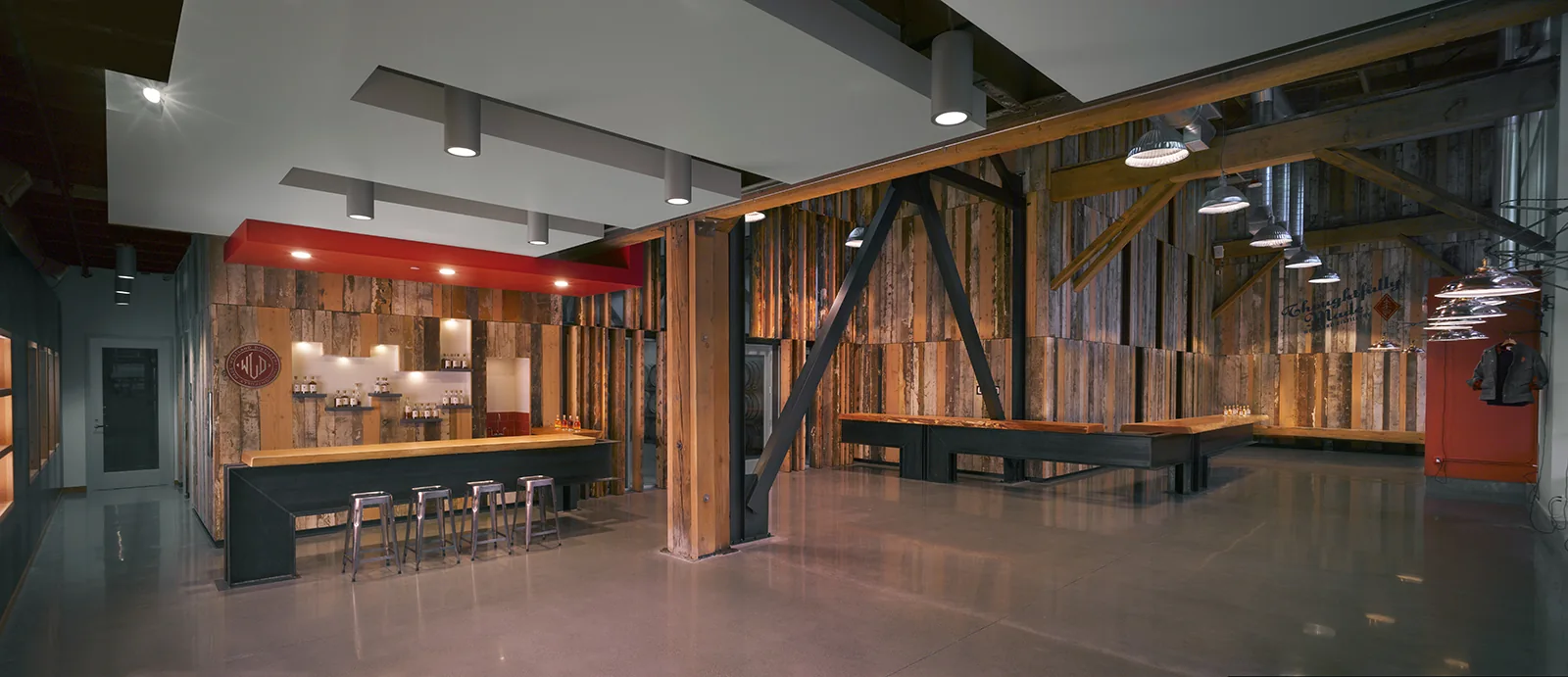Spacious industrial tasting room with reclaimed wood paneling, polished concrete floors, and steel structural beams.