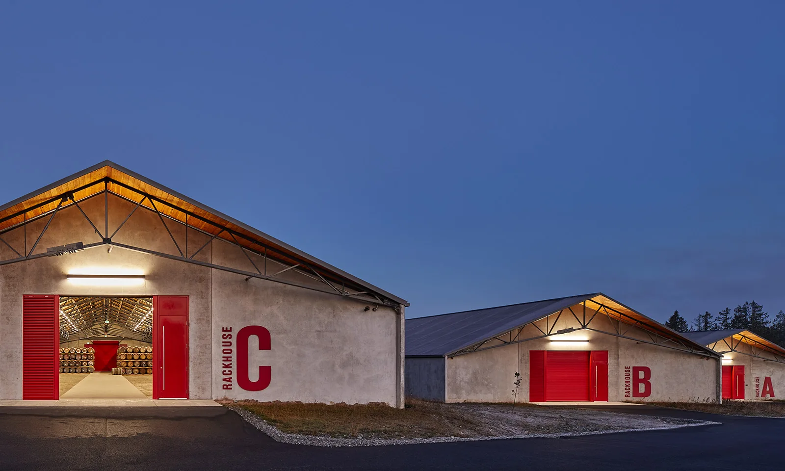 Three modern concrete rackhouses with bright red doors and large red lettering under a twilight sky.