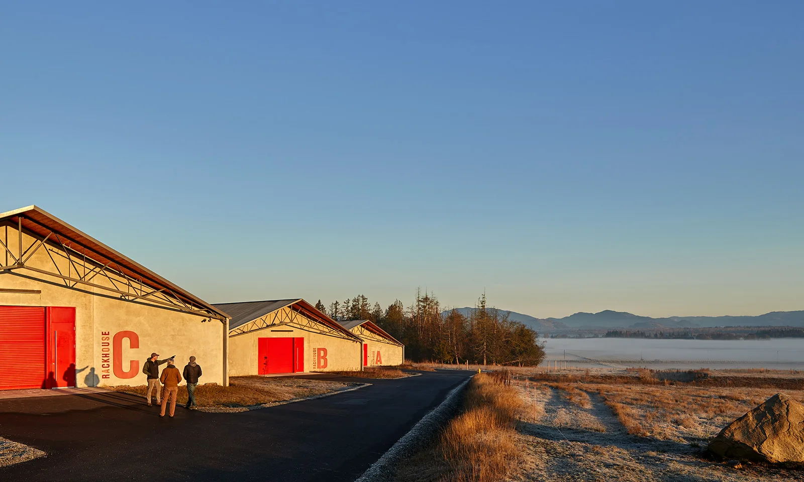 Three concrete rackhouses with red doors in a misty valley landscape, with three people standing outside.