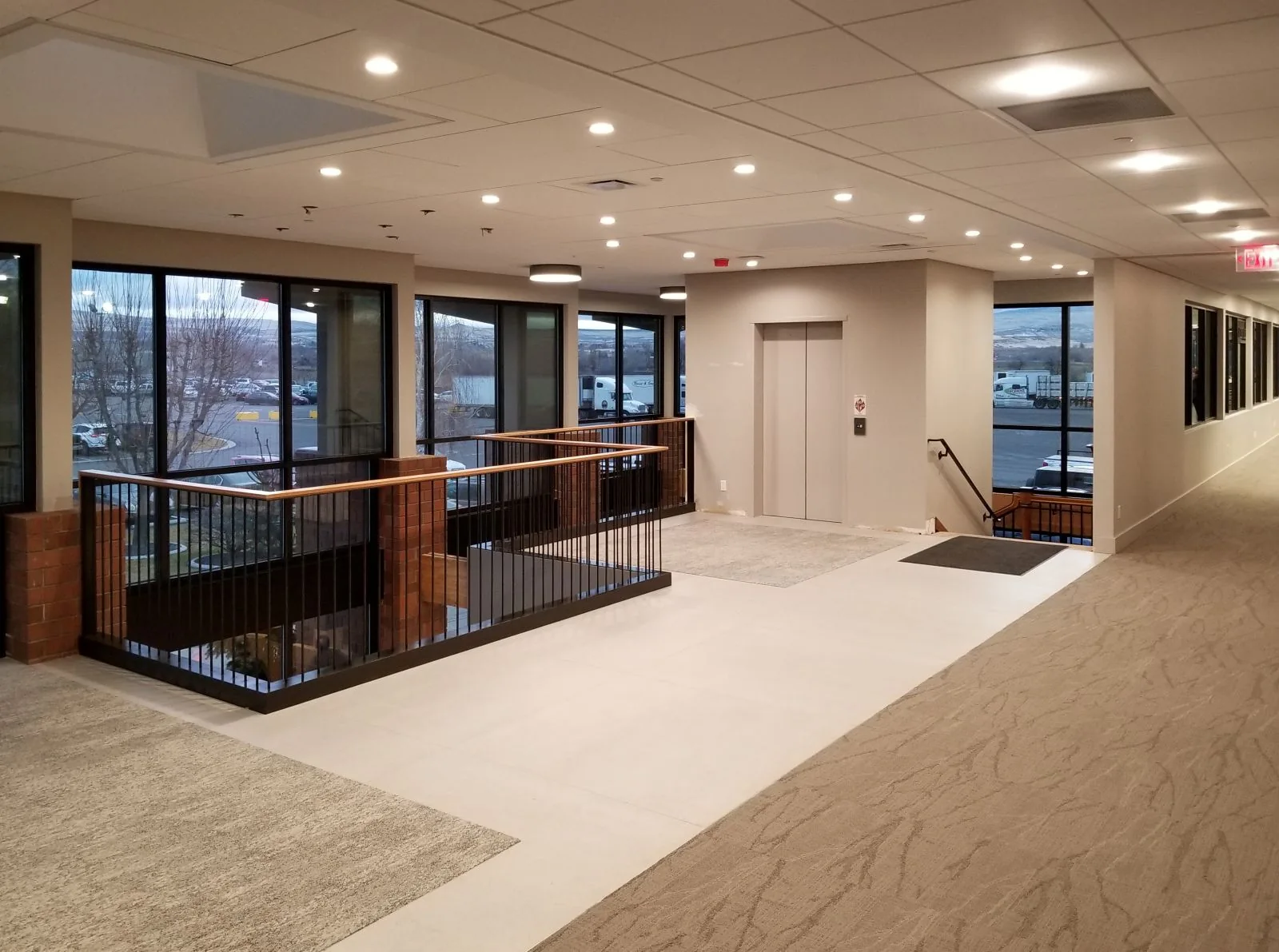 Bright office mezzanine featuring a staircase with wood railings, an elevator, and large windows.