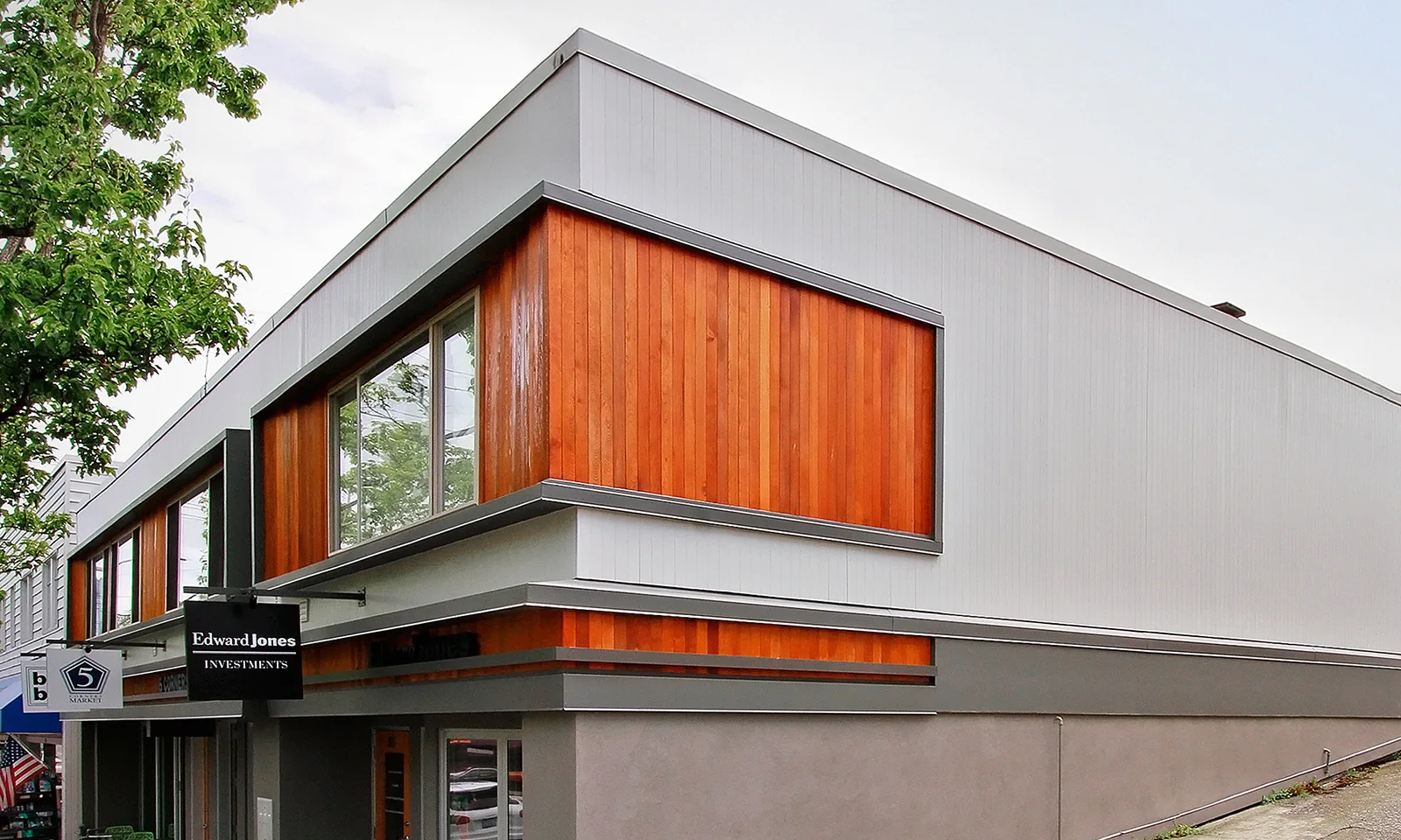 Modern commercial building exterior with light grey siding, warm vertical wood paneling, and large windows.