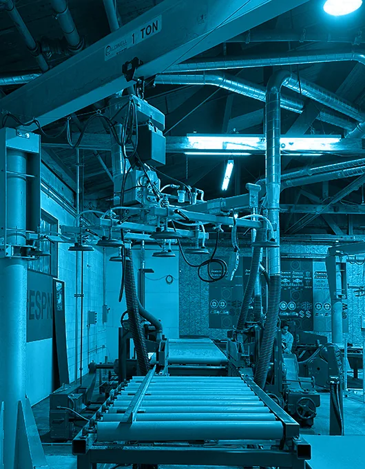 Industrial conveyor rollers and overhead crane machinery inside a factory, bathed in blue light.