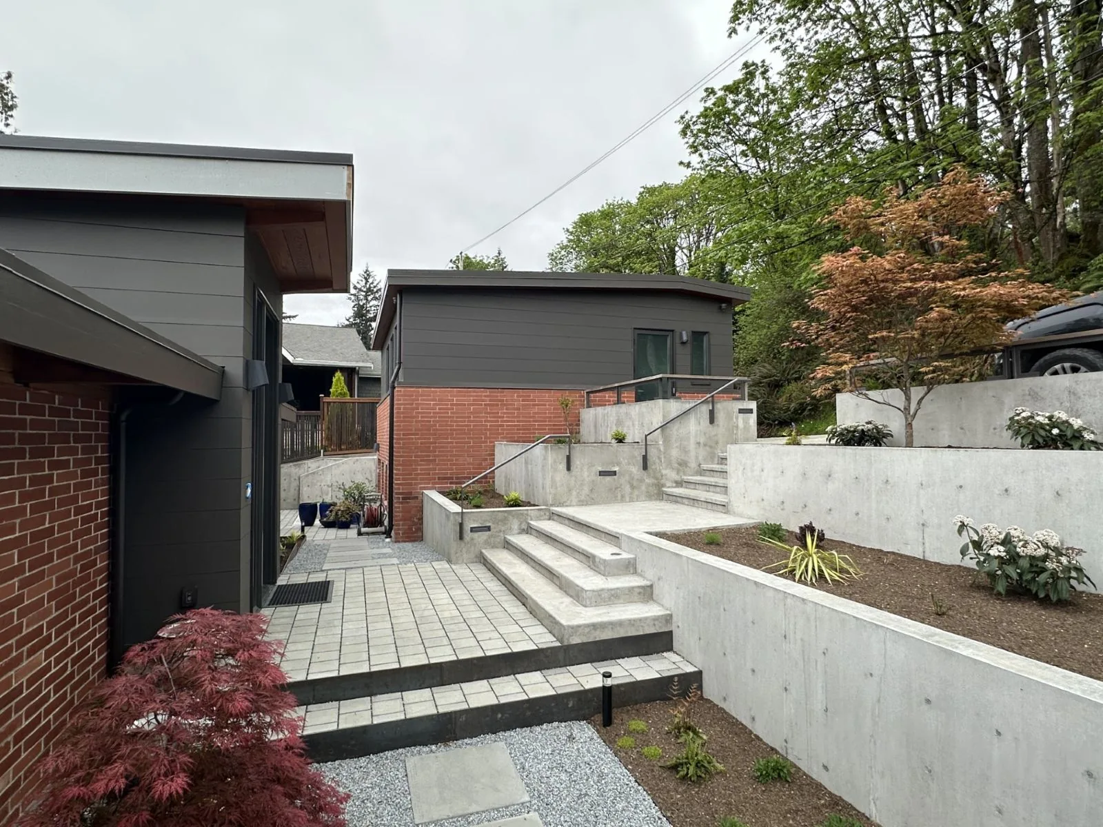 Modern backyard with tiered concrete retaining walls, stone steps, and dark grey siding on the home.